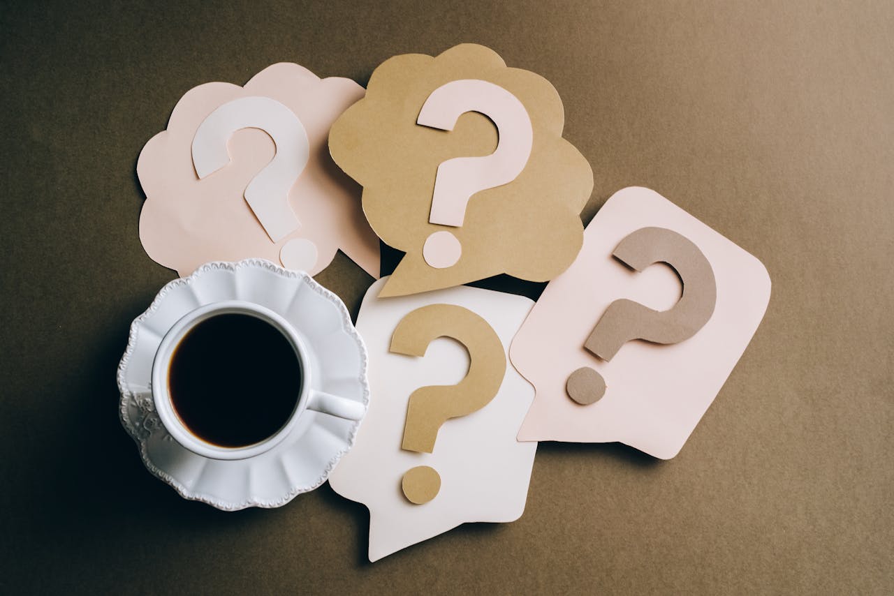 事業内容 Creative concept with coffee cup and paper question marks on a table.